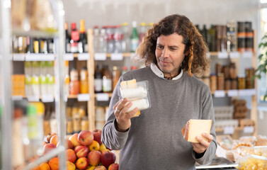 Adult man buyer chooses fresh cheese in grocery store