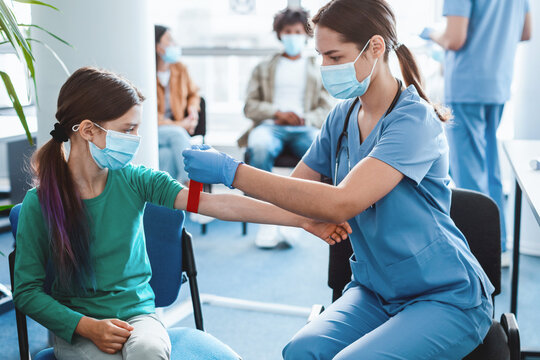 Concept of healthcare and medicine. Woman laboratory assistant in face mask preparing patient to do a blood analysis. Nurse tightening the medical tourniquet on arm before taking blood sample