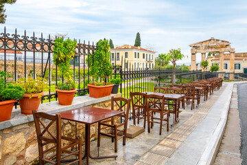 Sidewalk cafe tables lined up along the gate of the ancient Roman Arena with the Gate of Athena Archegetis behind, in Athens, Greece.
