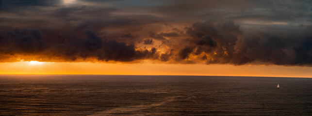Panoramic style photograph of sailboat and sunset over the Pacific Ocean horizon