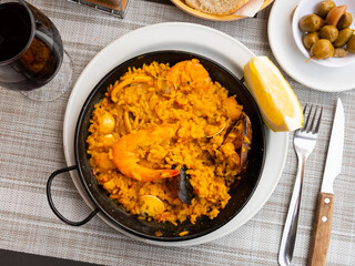 Portion of fresh seafood paella served on plate with piece of lemon.
