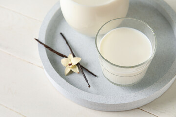 Glass of fresh vanilla milk with sticks and flower on white wooden background