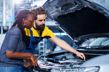 Mechanic at auto repair shop conducts annual vehicle checkup, informing customer about needed motor replacement. Garage employee talking with customer after finishing car inspection