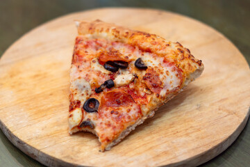 Trozo mordido de Pizza de pepperoni con aceitunas y champiñones sobre una tabla redonda de madera 