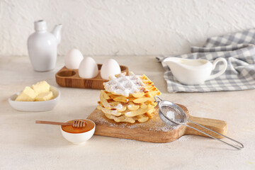 Delicious Belgian waffles with powdered sugar and honey on board on table against white background