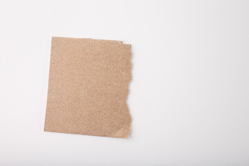 A piece of brown cardboard with a rough, torn edge placed on white background. Visible texture with small fibers. Supplies for craft project, step in creative process, recycled material, top view