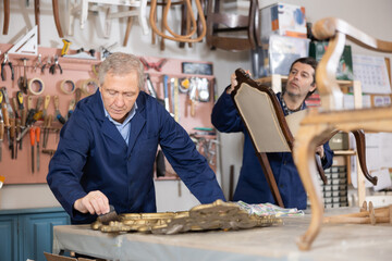 Employee of the restoration workshop treats the wooden frame of vintage mirror with a protective varnish