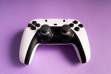A white and black gaming controller is centered on a bold purple background. The buttons,...