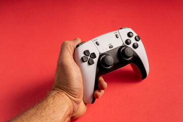 A hand firmly grips a white and black gaming controller against a bright red background. The buttons, joysticks, and design details are clearly visible, emphasizing a modern gaming experience.