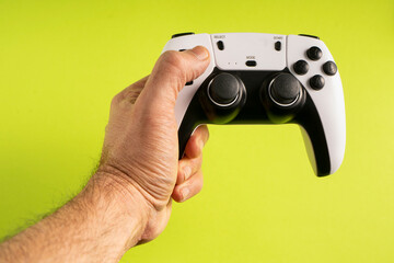 A hand firmly grips a white and black gaming controller against a bright green background. The buttons, joysticks, and design details are clearly visible, emphasizing a modern gaming experience.