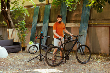 Obraz premium Sporty committed male cyclist taking care of his bikes in his yard maintaining and adjusting wheels with precision. Young caucasian man testing and servicing modern bicycle outdoor.