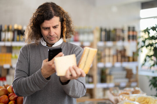 Adult man scans a barcode of a cheese package on his mobile. Buyer scans the QR code on his phone to pay at the supermarket checkout