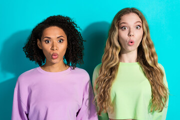 Two stylish young women expressing surprise against a vibrant turquoise background, showcasing...