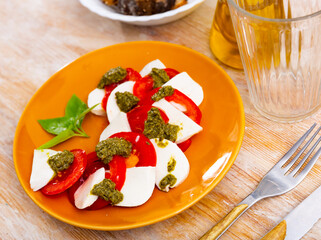 Fresh Italian caprese with mozzarella, tomatoes, basil leaves and pesto sauce