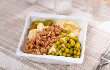 Spanish version of popular Russian salad from chopped boiled potatoes, eggs and carrots added with canned green peas and tuna served with olives