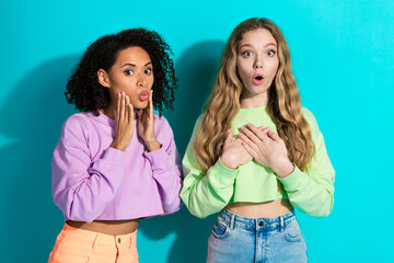 Two young women showing shocked expressions, wearing colorful sweatshirts against a vibrant teal...