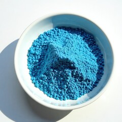 Sparkling blue sand particles scattered on a white background in a shallow dish, earthy, serene atmosphere, coastal