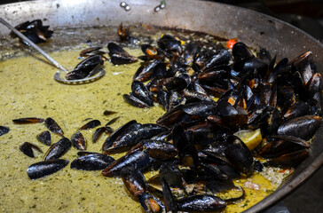 Delicious fresh mussels being cooked and presented in large pan with flavorful sauce. Seafood meal preparation for culinary delight, showcasing traditional cooking techniques