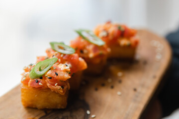 Delicious appetizer featuring salmon tartare on crispy bread with green garnish served on a wooden platter