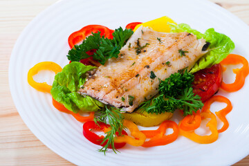 Delicious roasted juicy trout fillet served with fresh vegetables and greens