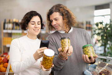 Checking expiration date of green olives - wife and husband shoppers scans QR code on label of jar canned olives using her smartphone