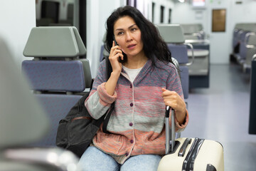 Fototapeta premium Portrait of smiling woman commuting in city using urban train and talking on smartphone
