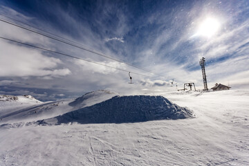 Snowy mountain ski lift under a radiant sun and dynamic clouds in winter
