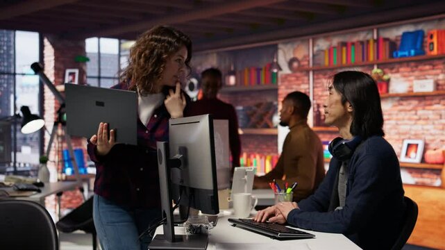 Startup intern holding laptop asks questions to senior technician coding advanced AI algorithm. Employee requests help from CTO manager in Silicon Valley workplace, camera B