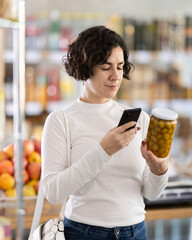 Woman scans barcode QR code on pickled olives label package, follows link and studies information for consumer in supermarket application. Client seek olives manufacturer data in on-line marketplace.