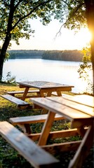 Naklejka premium A serene lakeside view with wooden picnic tables under trees during sunset.