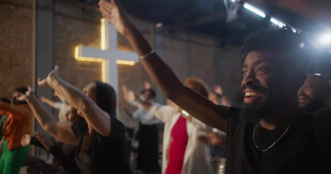 Diverse group raising hands in worship during church service, illuminated cross in background, expressions of praise, joy, and spiritual connection in community