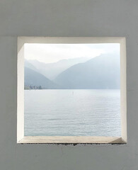 Scenic lake and mountain view framed by a white concrete window, creating a minimalistic and serene perspective with soft natural light and calming atmosphere.