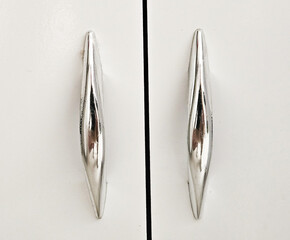 Handles on white wooden swing cabinet. Furniture accessories. Small silver furniture handles

