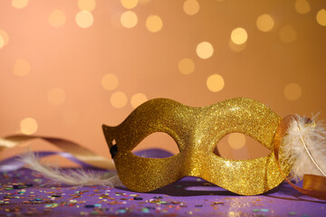 Beautiful carnival mask, ribbons and confetti on color background with blurred lights, closeup