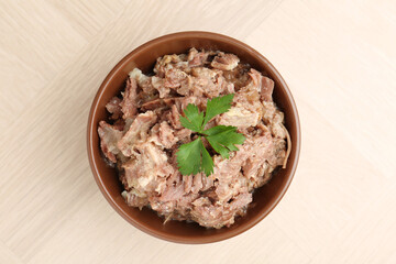 Canned meat with parsley in bowl on wooden table, top view