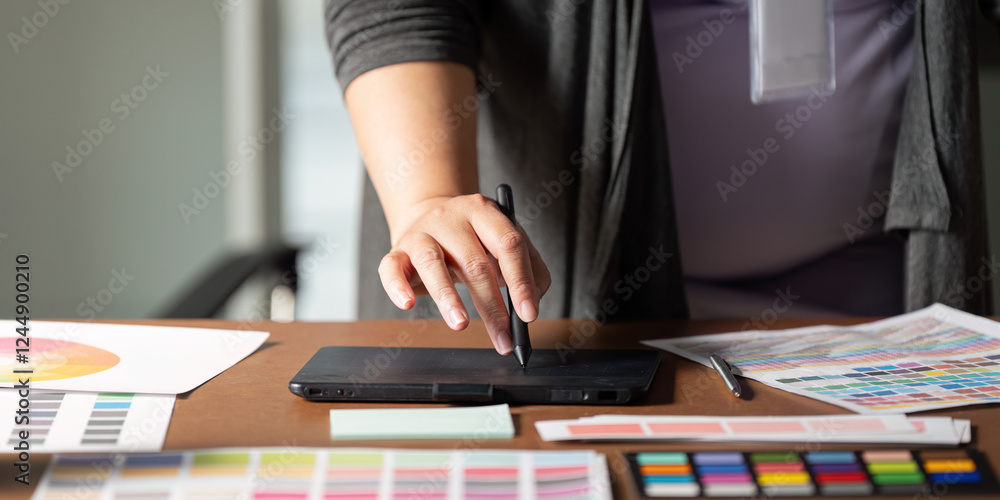 Aufkleber graphic designer using a digital tablet to create designs at a wooden workspace.