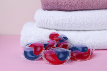 Laundry detergent capsules and clean towel on pink background, closeup