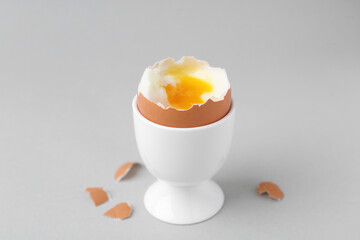 Soft boiled egg in cup and eggshell on light grey background