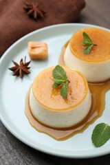 Tasty puddings with caramel sauce served on wooden table, closeup