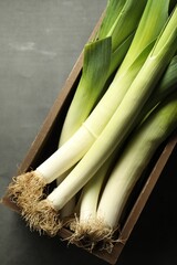 Fresh raw leeks in wooden crate on grey table, top view