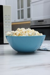 Tasty popcorn in bowl n on white marble table indoors