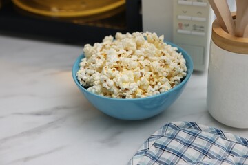 Tasty popcorn in bowl near microwave oven on white marble table, closeup