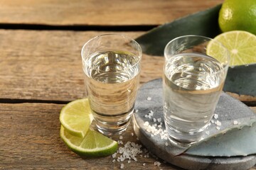 Tequila shots with salt, limes and agave leaves on wooden table, closeup
