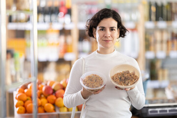 Woman choosing prepared oriental food yakisoba, doubt and think before buying. Client choose and decide purchase readymade food. Shop visitor pick up food in minimarket