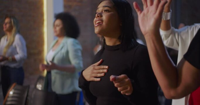 Young woman singing in worship with outstretched hand, expressing faith and devotion in church setting with illuminated cross, emotional spiritual connection