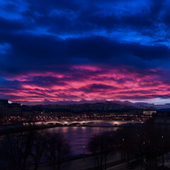 Cityscape at Night with Vibrant Pink and Purple Clouds Reflecting in the River below the Bridge.