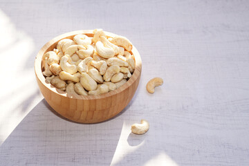 Cashew nuts in wooden bowl on white table with sunshine. Healthy food.