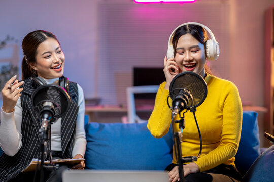 Two asian female podcasters recording audio content in home studio