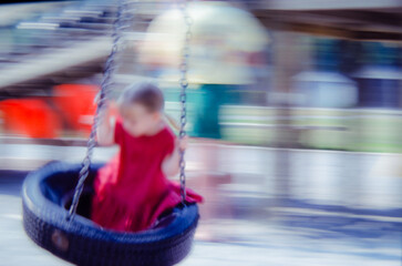 Young girl in a red dress on a tire swing with motion blur