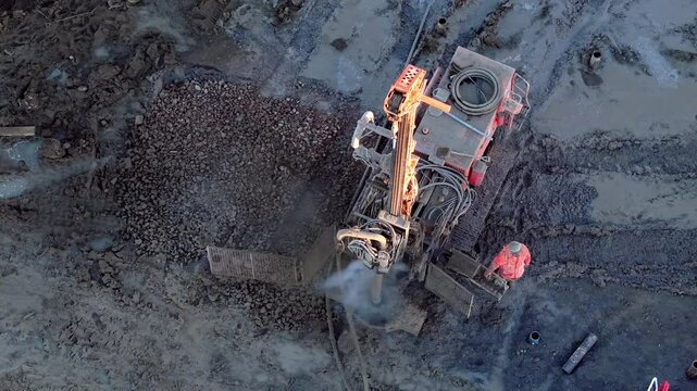 Aerial view from drone at Construction site shows heavy machinery drilling into ground with dust flying around